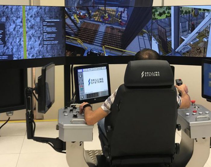 Persona que maneja un simulador de perforación con múltiples pantallas y paneles de control.