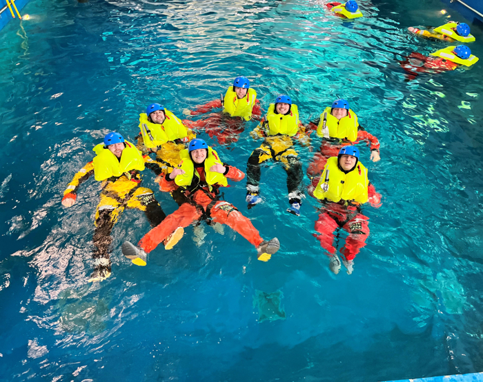 Siete individuos con trajes de flotación amarillo brillante y cascos azules flotan en una piscina, practicando técnicas de entrenamiento de seguridad o salvamento acuático tan precisas como las que realizan los militares.