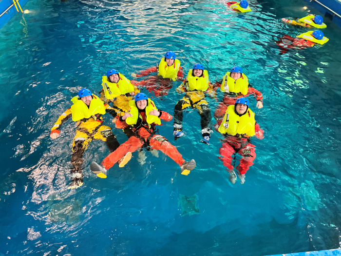 Siete individuos con trajes de flotación amarillo brillante y cascos azules flotan en una piscina, practicando técnicas de entrenamiento de seguridad o salvamento acuático tan precisas como las que realizan los militares.