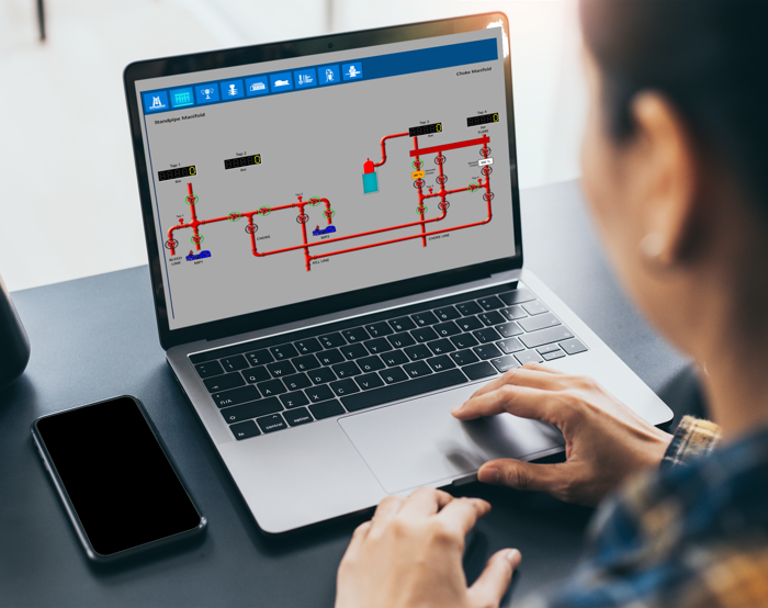 Una persona maneja un ordenador portátil que muestra un diagrama esquemático de un sistema técnico con tuberías e instrumentación. Sobre el escritorio hay un smartphone y una taza.