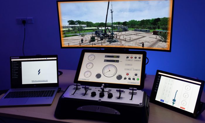 A workstation with two laptops, a central control panel, and a tablet displaying various data and interfaces. A large screen above shows an outdoor scene with machinery and structures.