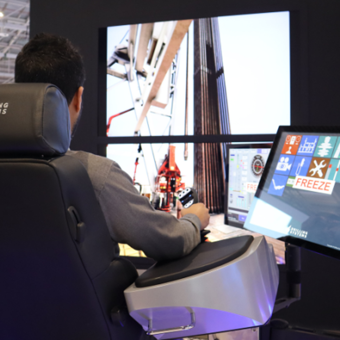 A person operates a drilling simulator with multiple screens displaying drilling operations, seated on a chair with the "Drilling Systems" logo next to a screen panel showing various control options.