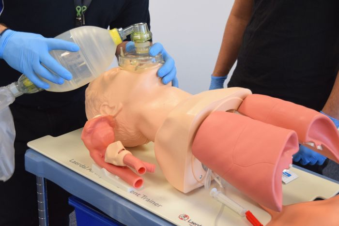 Dos individuos practican técnicas de RCP y ventilación en un torso de maniquí médico utilizando una máscara con válvula de bolsa.
