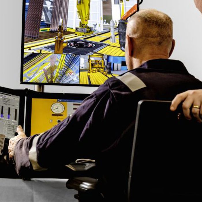 Two individuals in a control room, where one operates multiple monitors displaying various data and a construction scene.
