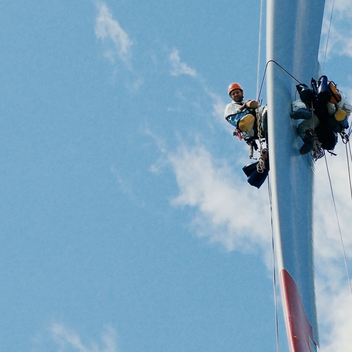 Two workers in safety gear, demonstrating their expert training, are suspended by ropes beside a wind turbine against a blue sky.