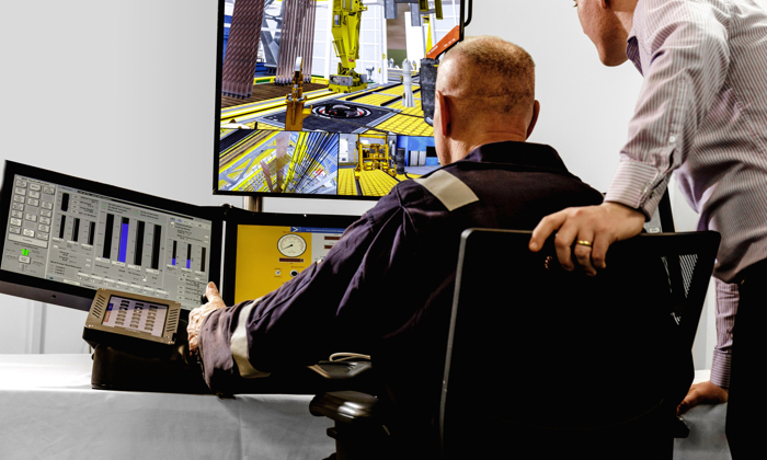 Dos personas observan e interactúan con datos y simulaciones en varios monitores en una sala de control. La escena incluye equipos industriales que aparecen en las pantallas.