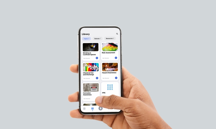 Una mano sostiene un smartphone que muestra una biblioteca de cursos relacionados con la seguridad, como Trabajo en espacios confinados, Evaluación básica y EPI, entre otros.