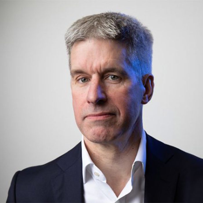 A man with short gray hair in a suit and white shirt poses against a light gray background.
