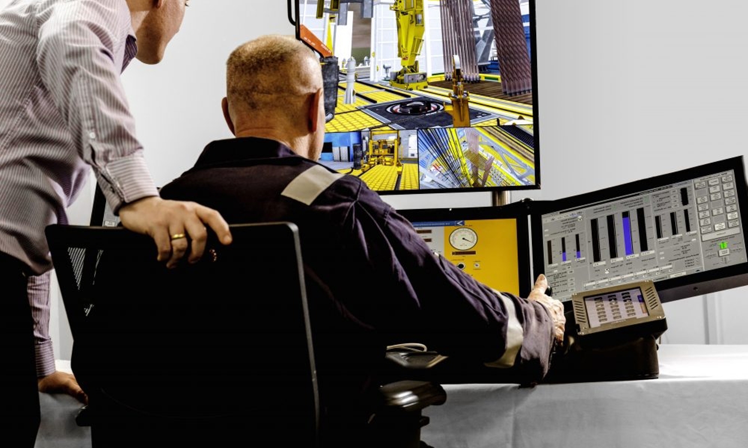 Dos hombres en una sala de control supervisan varias pantallas que muestran maquinaria industrial y gráficos de datos. Uno de ellos está sentado y el otro, inclinado, observa las pantallas.