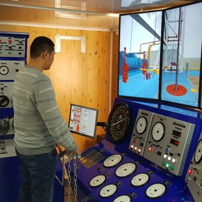 Person operating a training simulator for drilling systems, featuring multiple control panels and a digital display showing a drilling rig scenario.