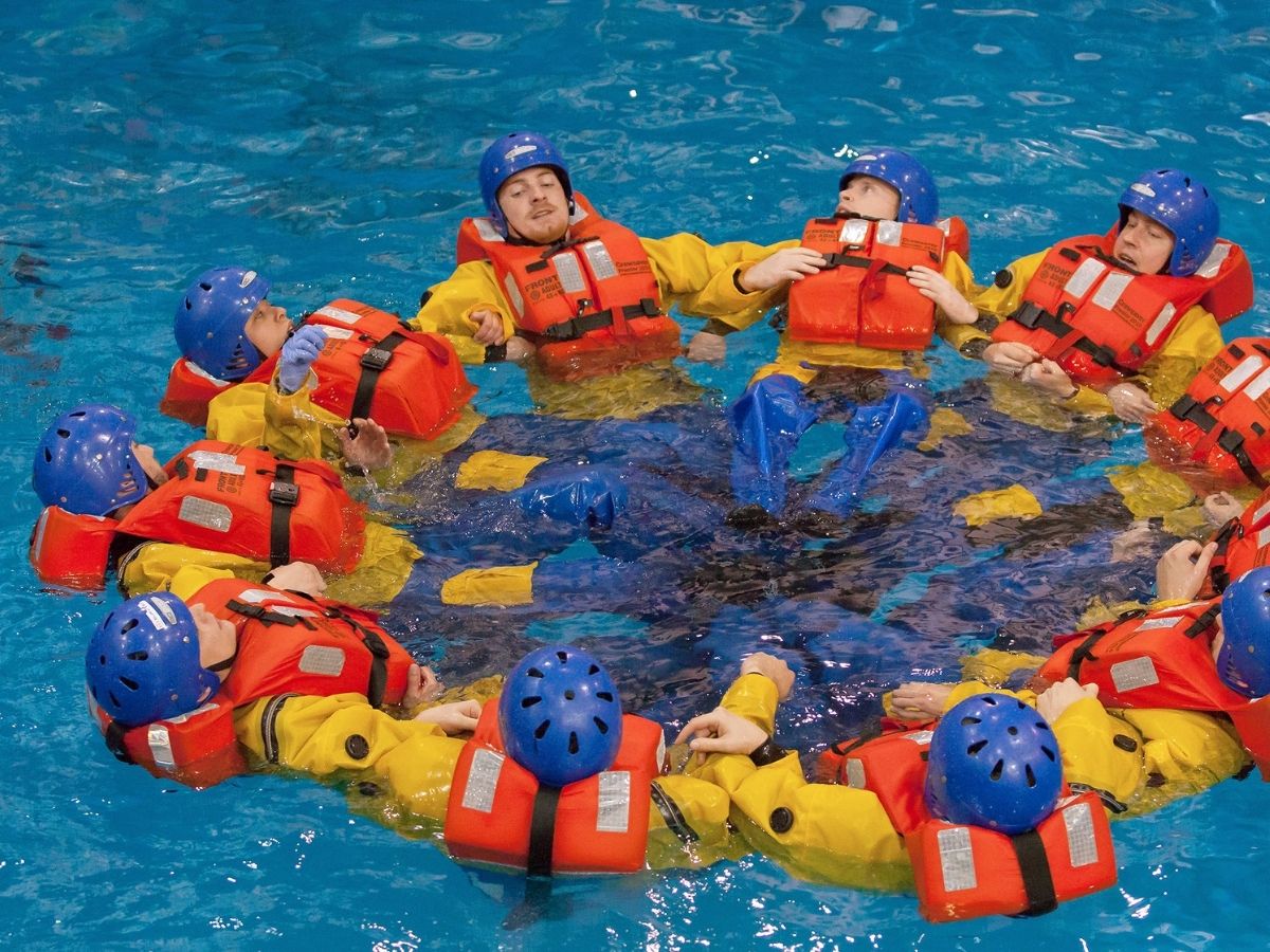 GWO sea survival training - delegates in yellow survival suits, life jackets and blue helmets are holding onto each other in a circle in a pool.