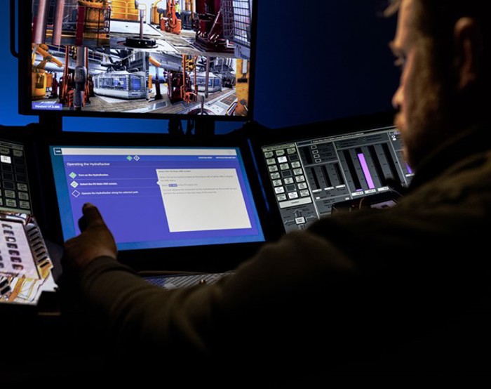 A person operates equipment using various screens, including one showing images of machinery and another displaying digital data and controls.