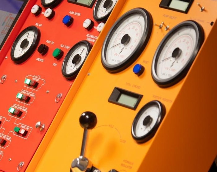 Primer plano de dos paneles de control, uno rojo y otro amarillo, con varios diales, interruptores, botones y medidores, que indican la instrumentación de maquinaria o equipos técnicos.