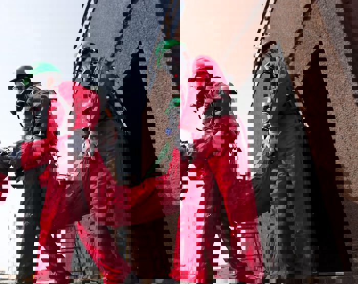 Efectivos de emergencias con trajes protectores rojos y cascos verdes suben a una persona por una escalera metálica.