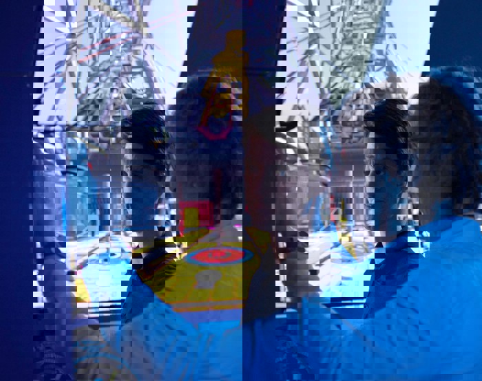 Dos hombres en una sala de control manejan un simulador con una gran pantalla que muestra el interior de un entorno industrial. Uno señala mientras el otro observa atentamente.