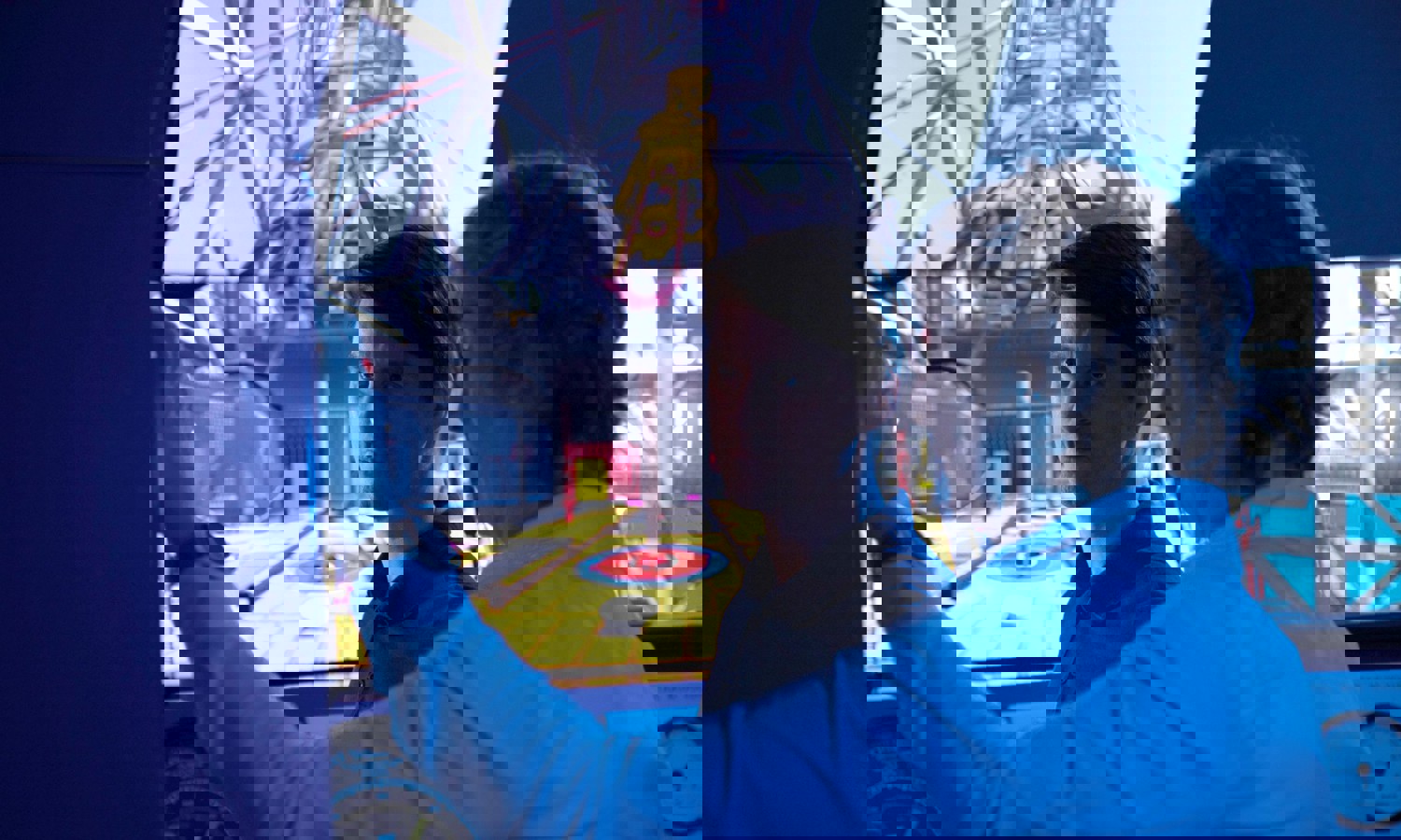 Dos hombres en una sala de control manejan un simulador con una gran pantalla que muestra el interior de un entorno industrial. Uno señala mientras el otro observa atentamente.